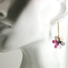 Pink, tan and black and white stone flower earrings hanging from long gold fill earwire on a mannequin ear.