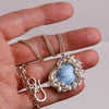 Turquoise heart pendant surrounded by clustered pearls on a silver chain held in hand for size.