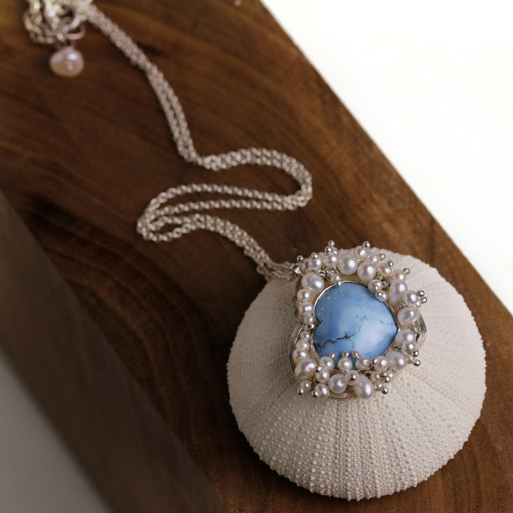Turquoise heart pendant surrounded by clustered pearls on a silver chain.