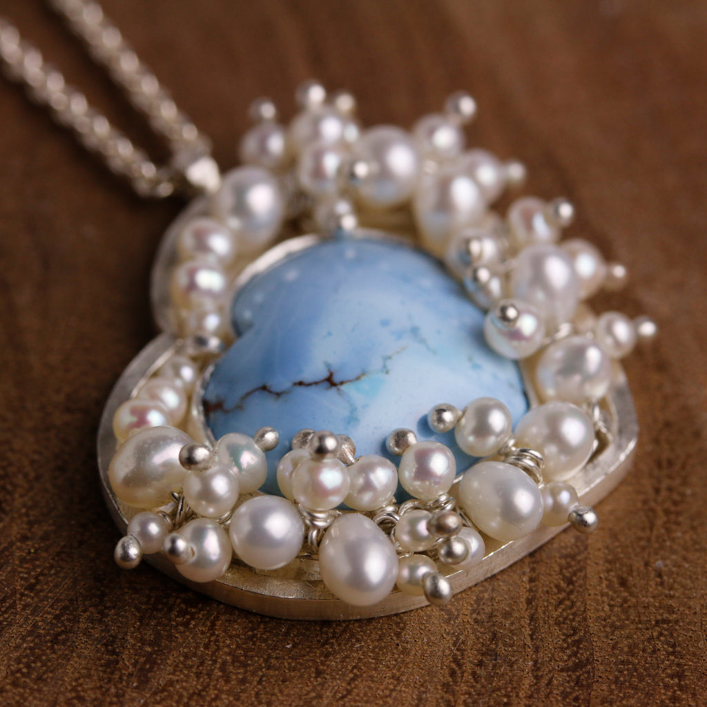 close up of Turquoise heart pendant surrounded by clustered pearls.