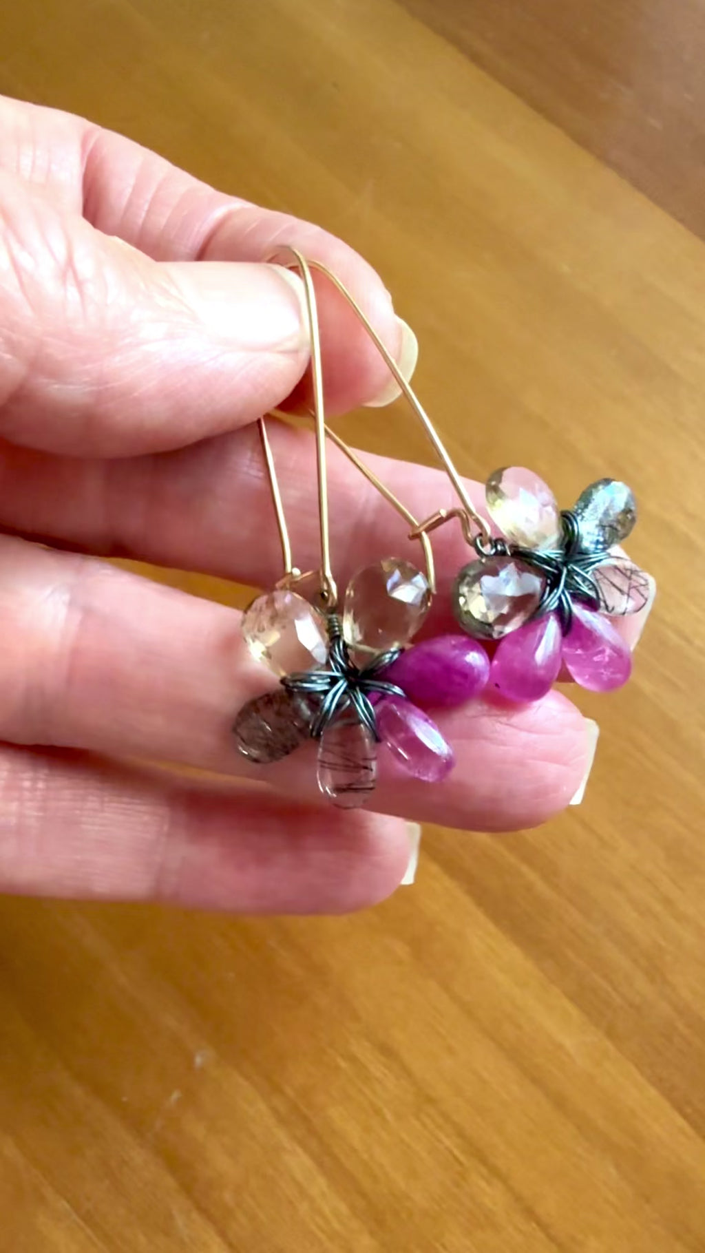 Video of fingers holding pink sapphire flower earrings and moving them back and forth in the light to sparkle.