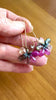 Video of fingers holding pink sapphire flower earrings and moving them back and forth in the light to sparkle.
